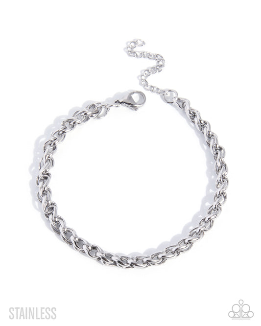 A silver stainless steel curb chain bracelet with a lobster clasp and extender chain, displayed on a clean white background with 'STAINLESS' text in the lower left and a small logo in the lower right.