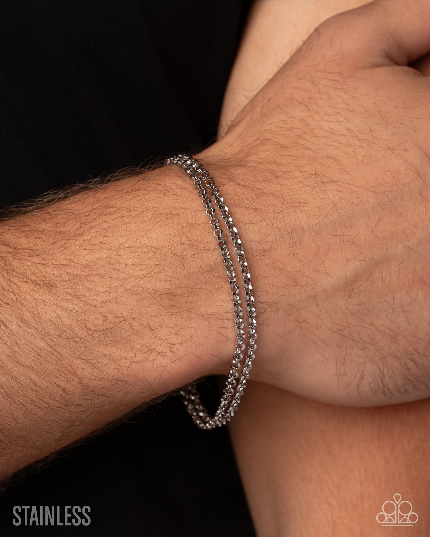 A close-up of a person's wrist wearing a double-strand silver stainless steel beaded chain bracelet against a black shirt background.