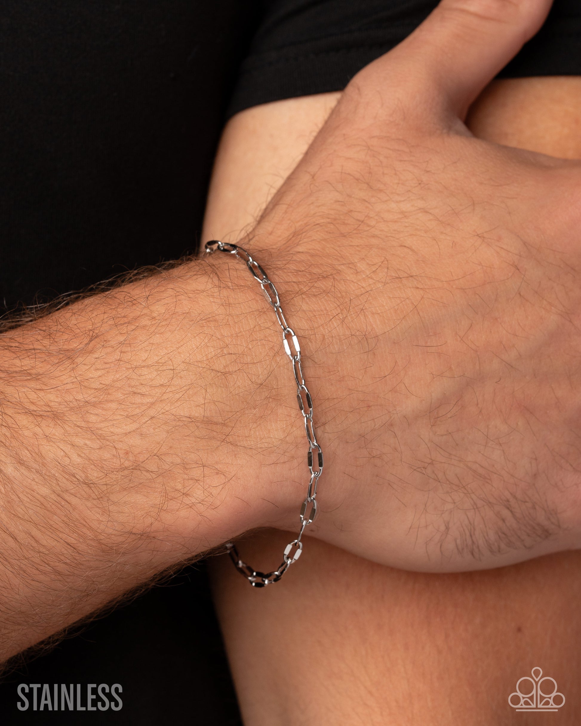 A close-up of a person's wrist wearing a polished stainless steel paperclip chain bracelet, with the word 'STAINLESS' in the bottom-left corner.