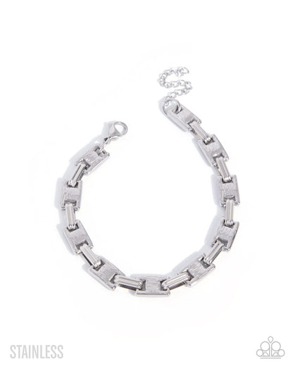 A silver stainless steel link chain bracelet with a textured, brushed finish on the larger rectangular links and a polished clasp, displayed on a clean white background with 'STAINLESS' text in the bottom left and a small logo in the bottom right.