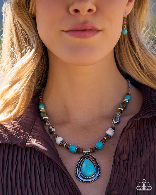 A close-up lifestyle shot of a woman wearing a turquoise and silver beaded necklace with a teardrop pendant, matching drop earrings, and a brown pleated top.