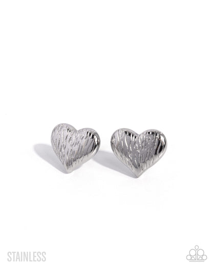 A pair of silver heart-shaped stud earrings with a textured, brushed stainless steel finish, displayed on a clean white background.