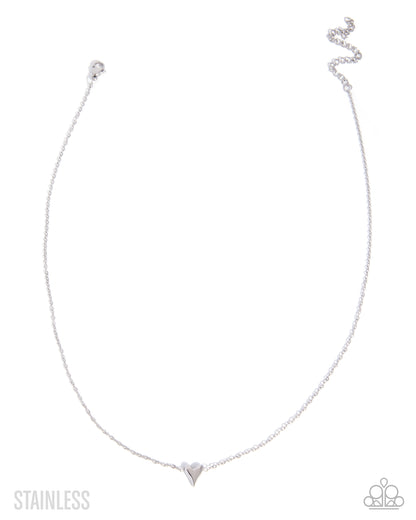A delicate stainless steel chain necklace with a small heart-shaped pendant, displayed on a clean white background with a brand logo in the bottom right corner.