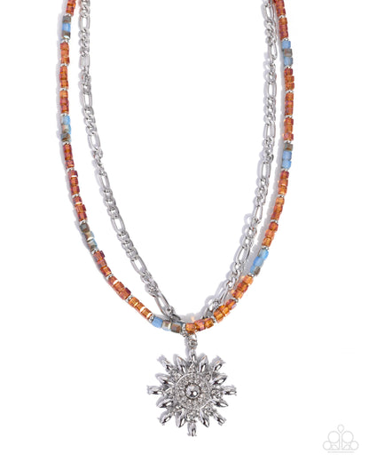 A double-strand necklace featuring a silver-tone sunburst pendant, a silver chain, and a beaded strand with orange, light blue, and gray beads on a white background.