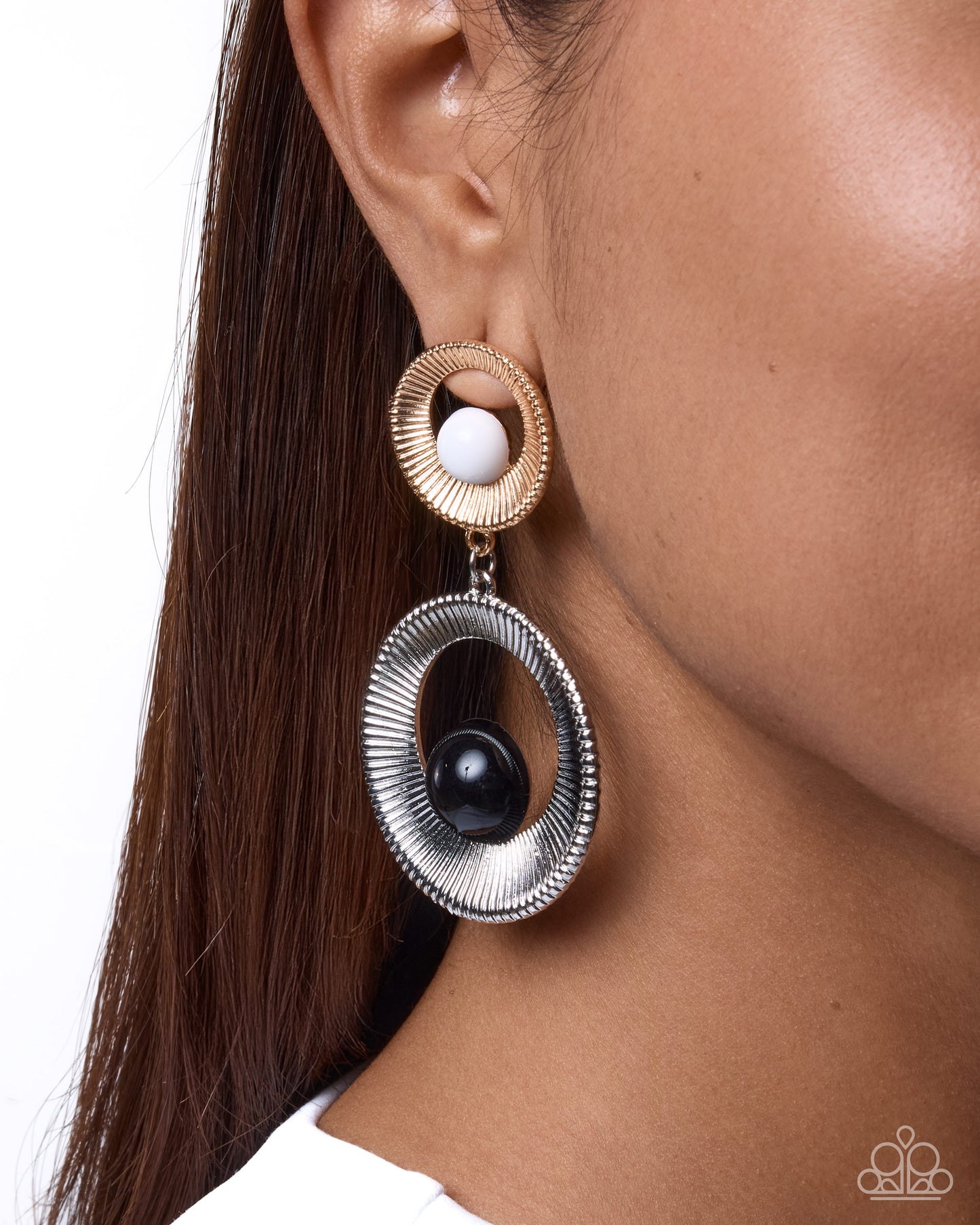 A close-up of a model's ear wearing a statement dangle earring. The earring features a textured gold-toned top ring with a white pearl, connected to a larger textured silver-toned oval drop with a black pearl at the center.
