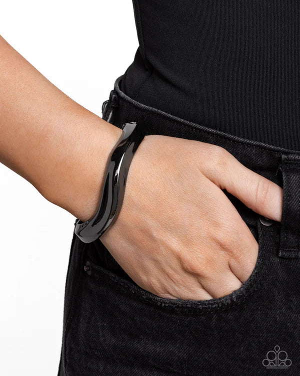 Person wearing a black outfit with a large metallic bracelet on a white background