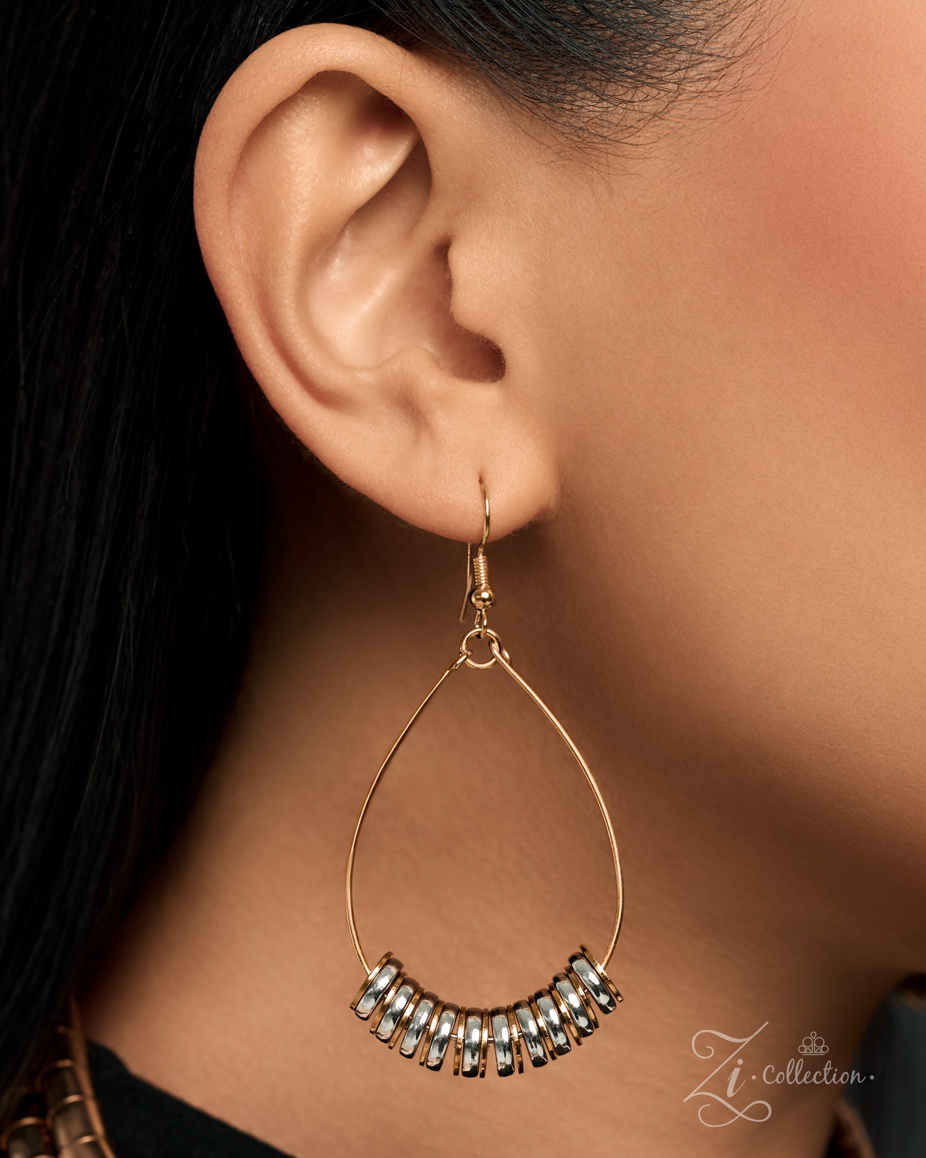 A close-up of a model's ear wearing a gold teardrop hoop earring with a curved row of clear rhinestones at the bottom. The image features a watermark logo for 'Zi Collection' in the bottom right corner.