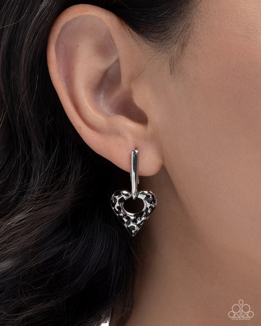 Silver heart-shaped earring worn by a person with dark hair.