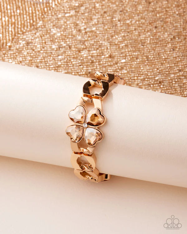 Rose gold bracelet with clover-shaped charms on a beige surface