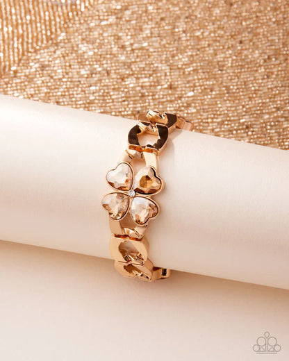 Rose gold bracelet with clover-shaped charms on a beige surface