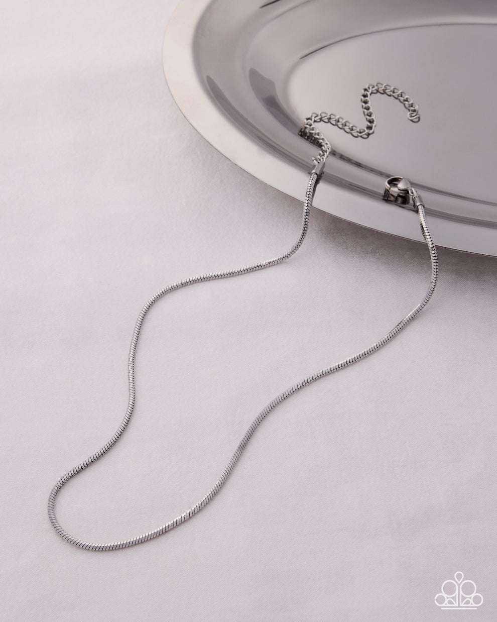 Silver necklace on a light gray surface with a silver dish in the background