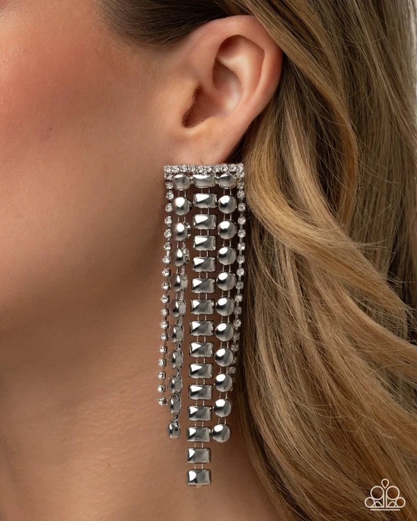 A close-up of a model's ear wearing a long, dangling statement earring made of multiple cascading strands of silver-toned rhinestones.