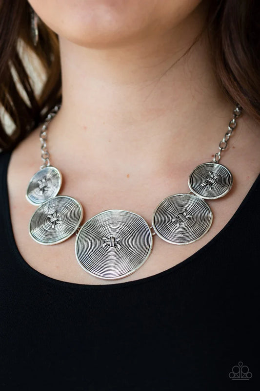 Silver necklace with circular pendants on a person wearing a black top.