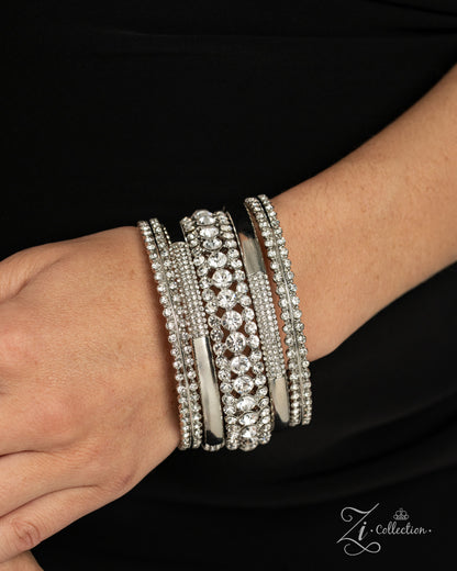 A close-up of a person's wrist wearing a stack of wide silver bangles adorned with clear rhinestones and crystal-like stones, set against a black top background. A 'Zi Collection' logo watermark is visible in the bottom right corner.
