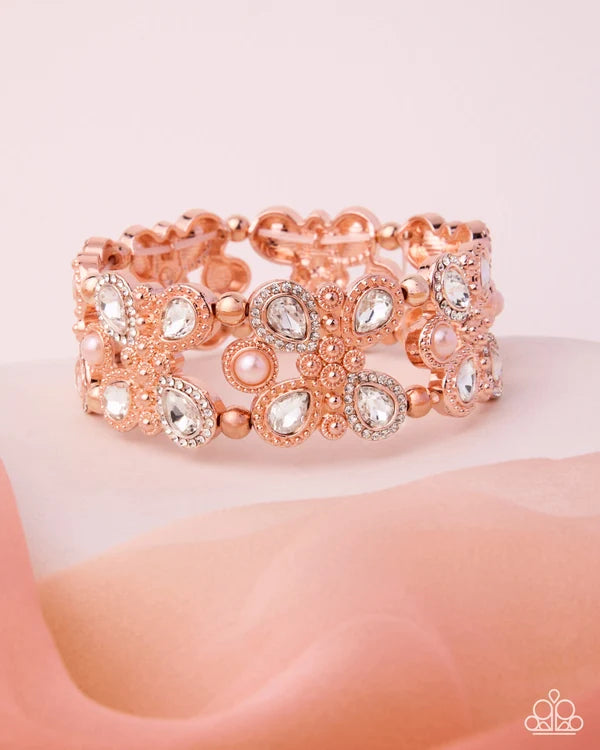 A rose gold cuff bracelet adorned with clear crystals, faux pearls, and small gold beads, displayed on a soft pink fabric surface.