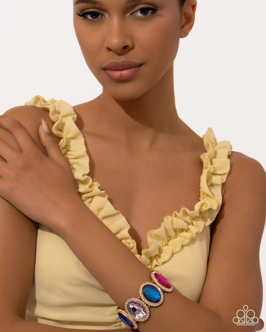 Woman wearing a yellow ruffled top with colorful gemstone bracelets on a plain background