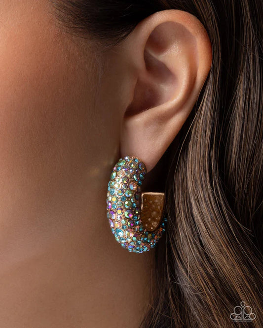 Close-up of an ear wearing a sparkling gold hoop earring with multicolored stones.