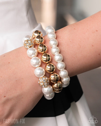 Close-up of a wrist wearing multiple pearl and gold bracelets with a blurred background.
