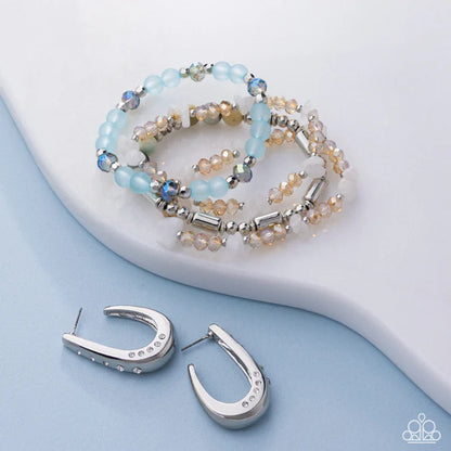 Beaded bracelet and silver hoop earrings on a light blue surface with a white background