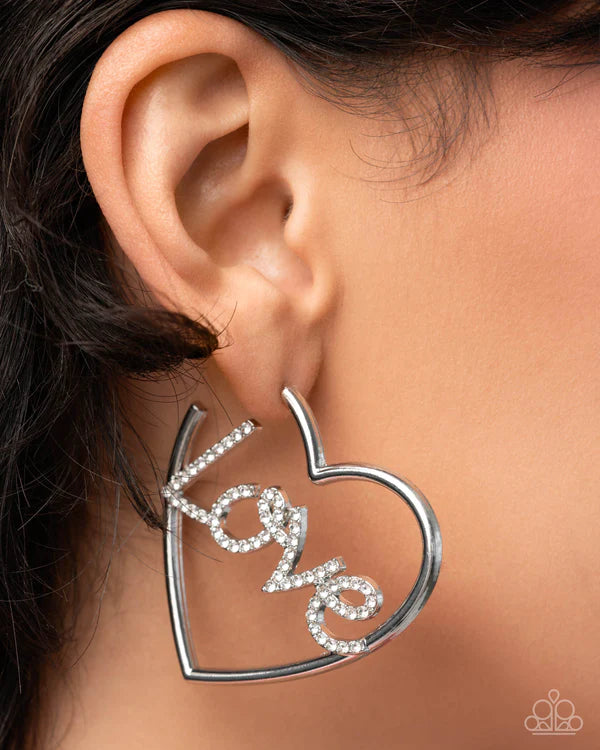 Heart-shaped earring with 'LOVE' inscription worn by a person