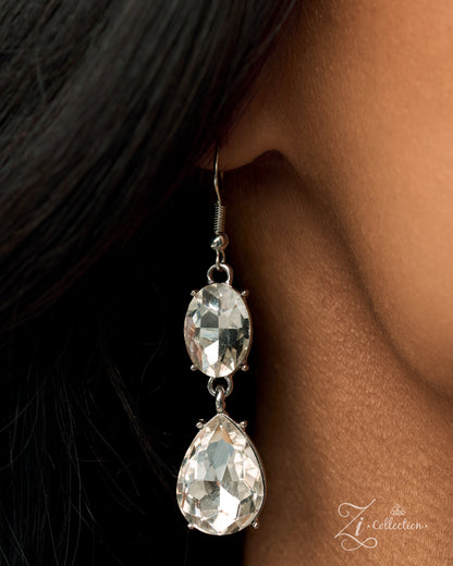 A close-up of a model's ear wearing a silver-toned double drop earring with clear faceted teardrop and oval crystals, set against dark hair and skin.