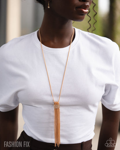 Person wearing a long gold necklace with tassels on a white shirt.