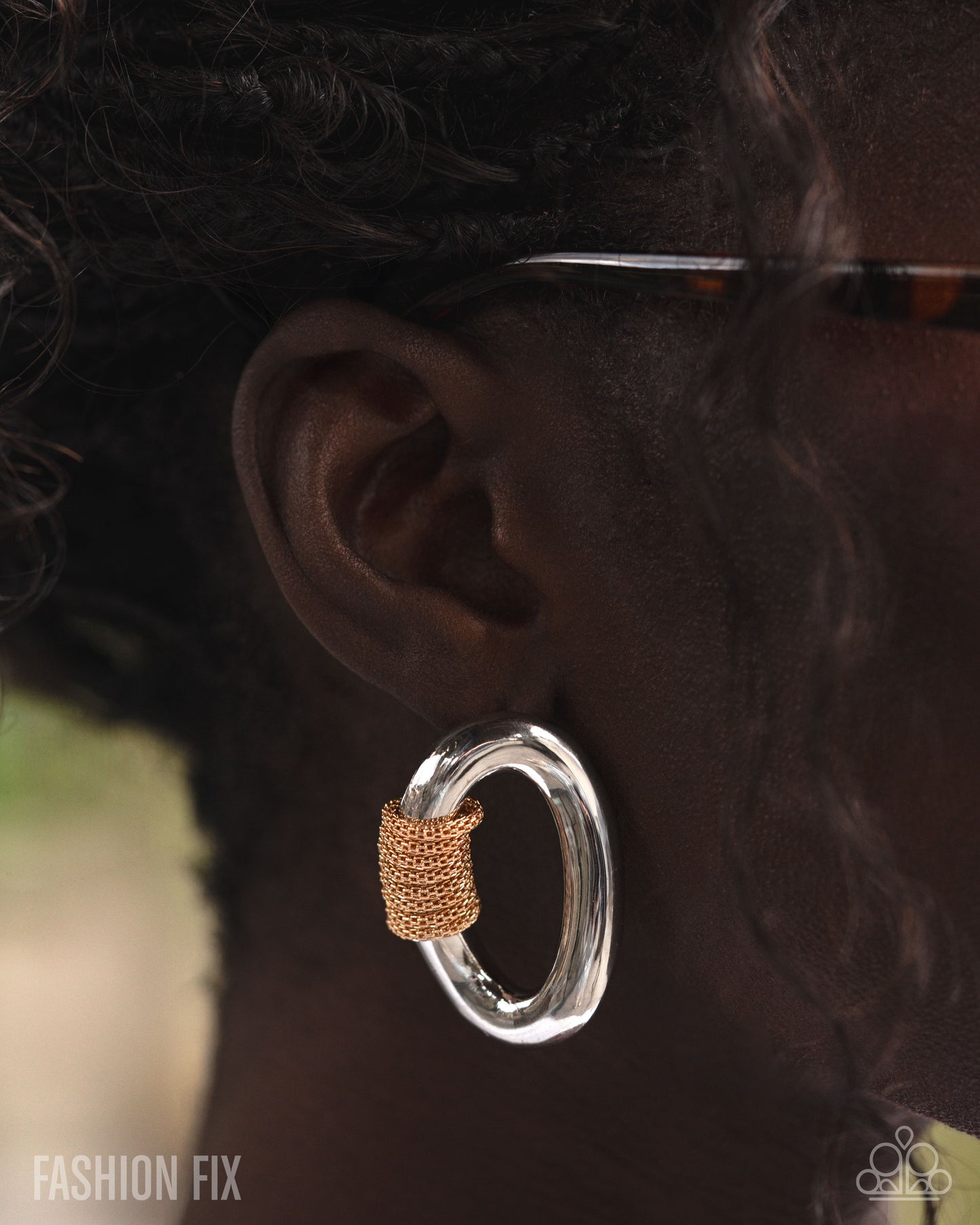 Close-up of an ear wearing a silver hoop earring with a gold accent, blurred background.