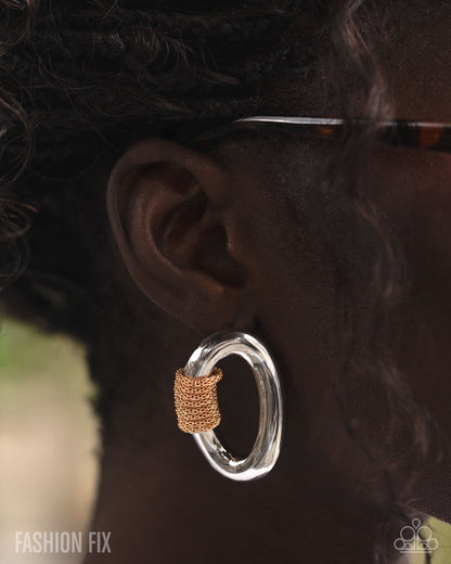 Close-up of an ear wearing a silver hoop earring with a gold accent, blurred background.