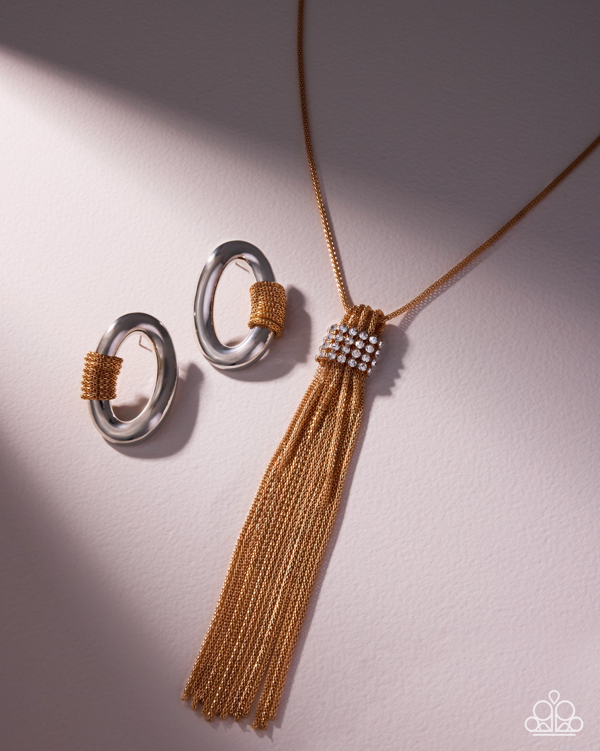 Gold necklace with tassel and silver rings on a light gray background