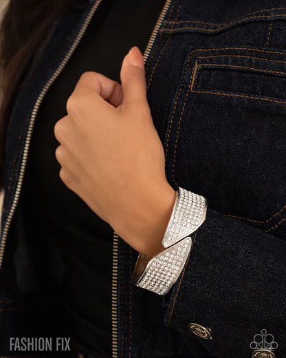 Hand wearing a silver bracelet on a dark denim background