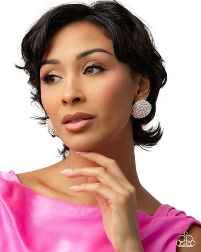 Woman wearing large, round earrings with a pink top against a white background