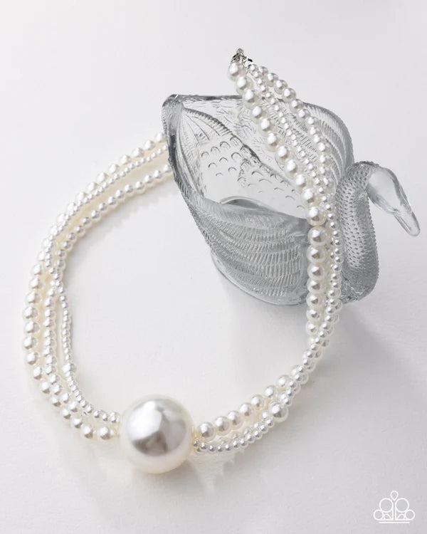 Pearl necklace draped over a silver teacup on a white background