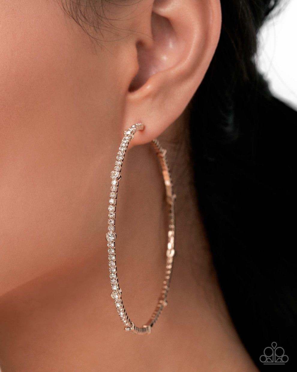 Rose gold hoop earring with clear stones worn by a person