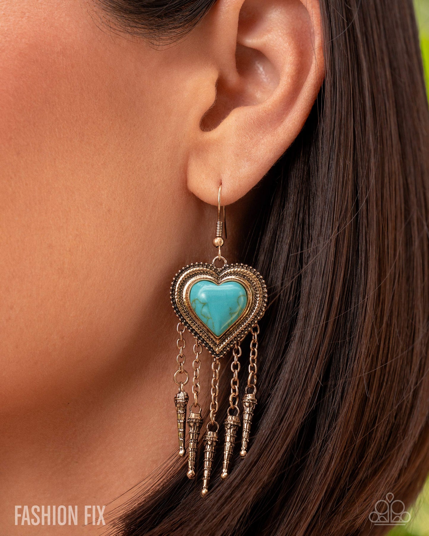Turquoise heart-shaped earring with dangling elements worn by a person.