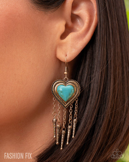 Turquoise heart-shaped earring with dangling elements worn by a person.