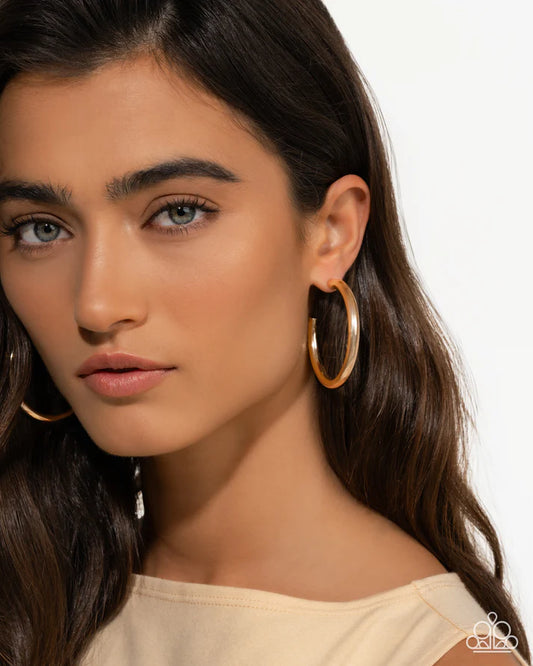 Close-up of a woman wearing gold hoop earrings with a neutral background