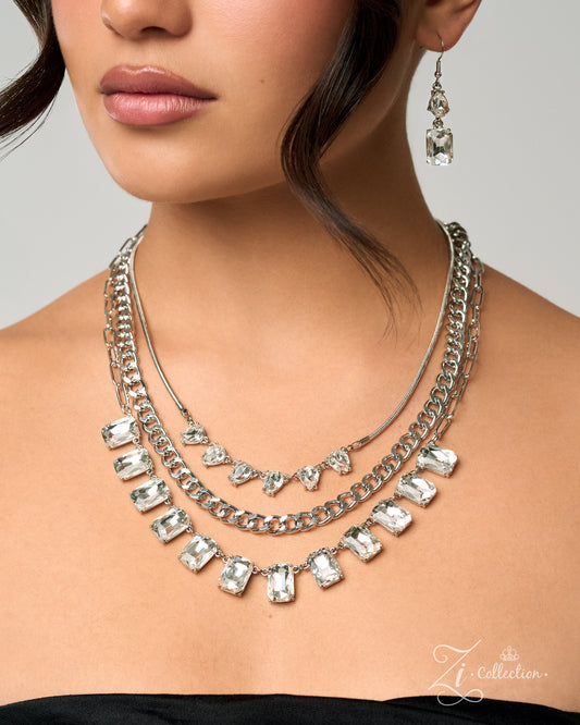 A close-up of a model wearing a multi-layered silver necklace with clear rectangular and heart-shaped rhinestones, along with matching dangling earrings, against a light gray background.