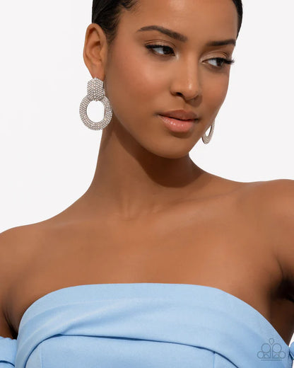 Woman wearing large hoop earrings with a plain background