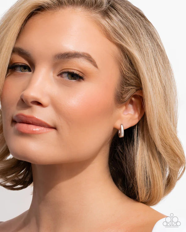 Close-up of a woman wearing a silver hoop earring on a plain background