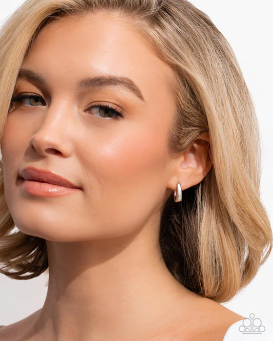 Close-up of a woman wearing a silver hoop earring on a plain background
