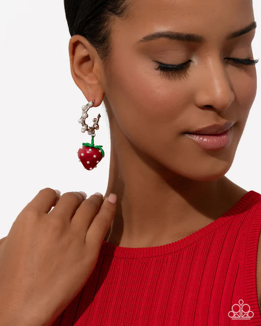 Close-up of a woman wearing a strawberry-themed earring with a plain background