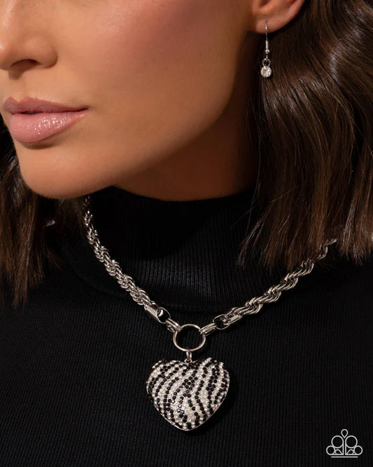 Close-up of a person wearing a silver chain necklace with a heart-shaped zebra print pendant.