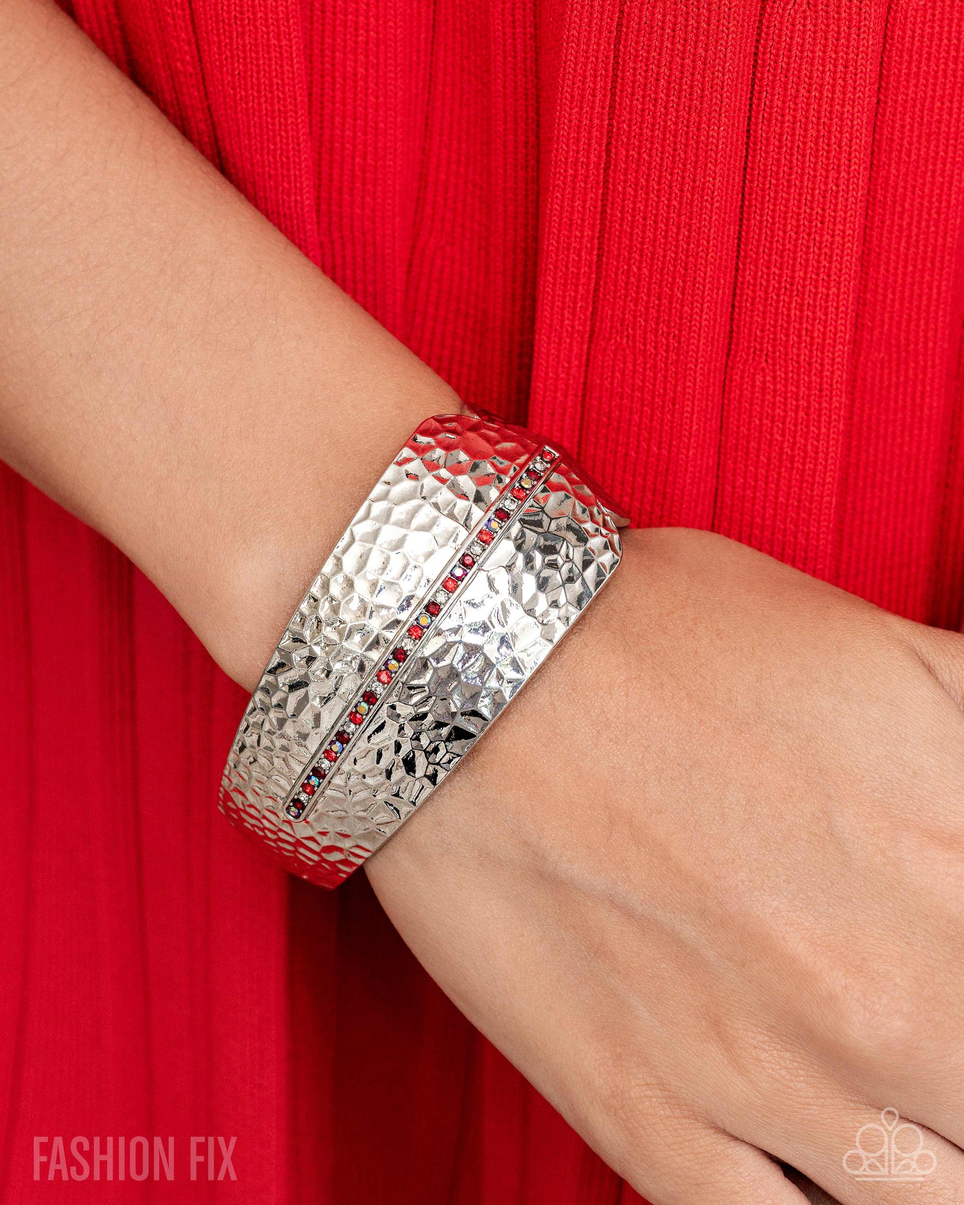 Silver bracelet with red stones on a wrist against a red background