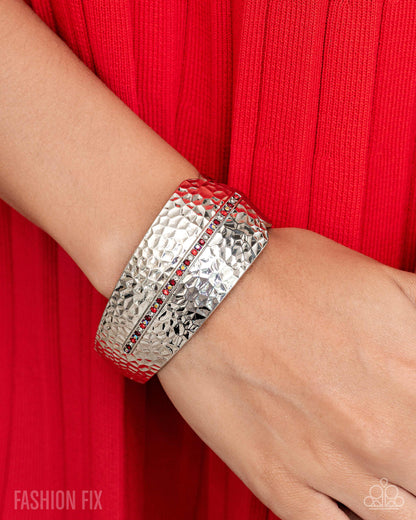 Silver bracelet with red stones on a wrist against a red background