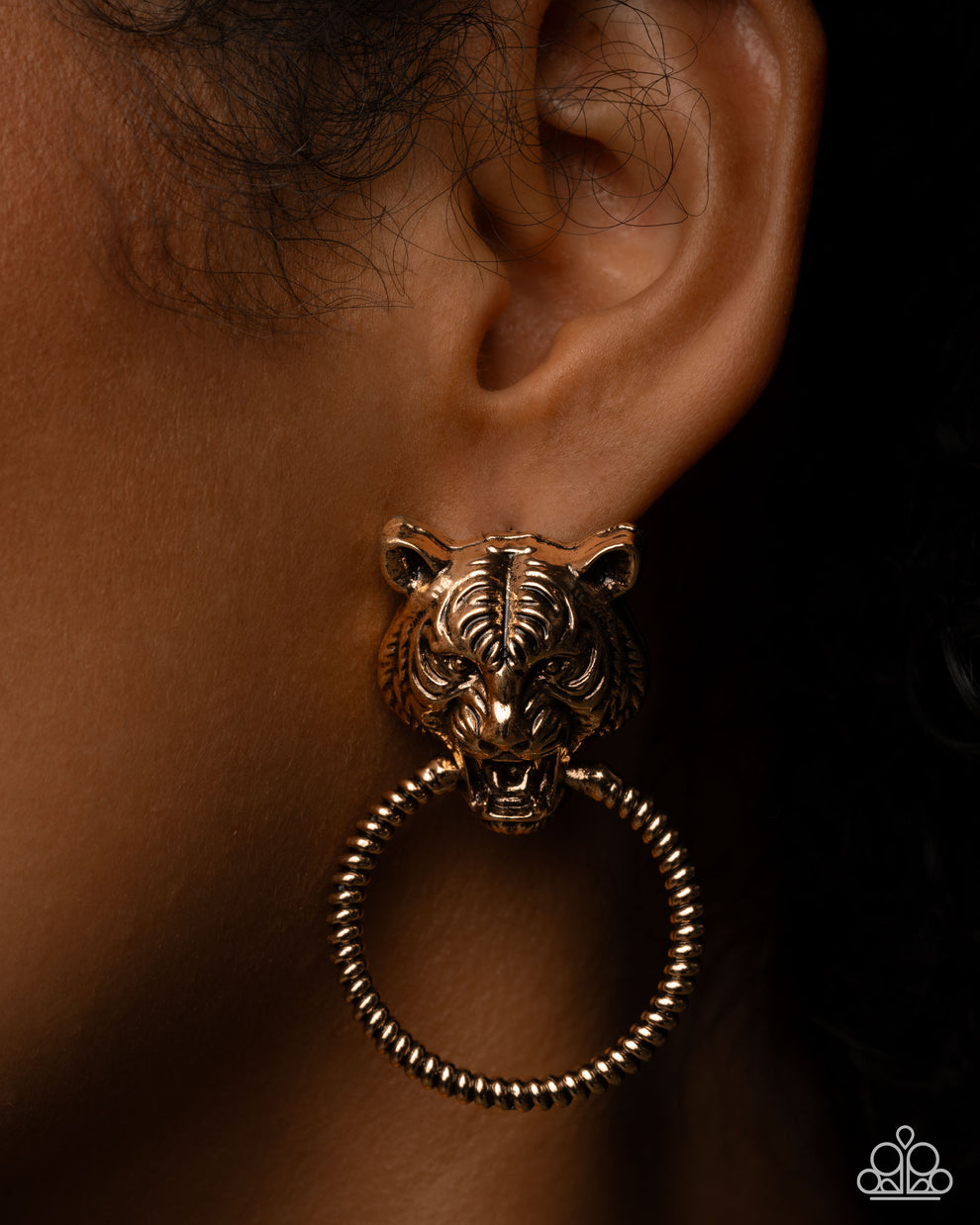Gold tiger-shaped earring on an ear with a dark background