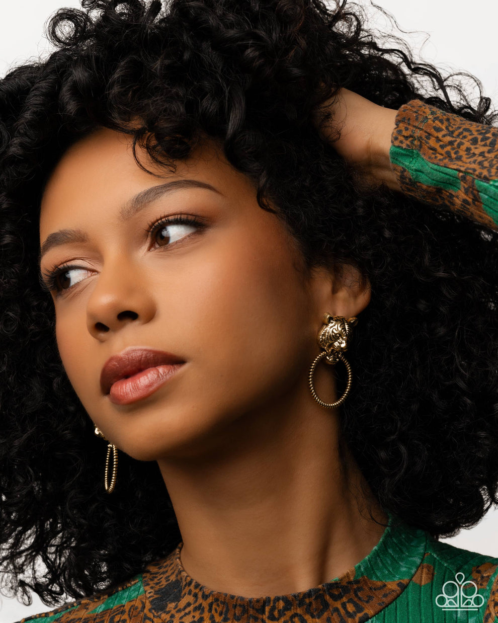 Woman with styled hair wearing gold hoop earrings against a neutral background