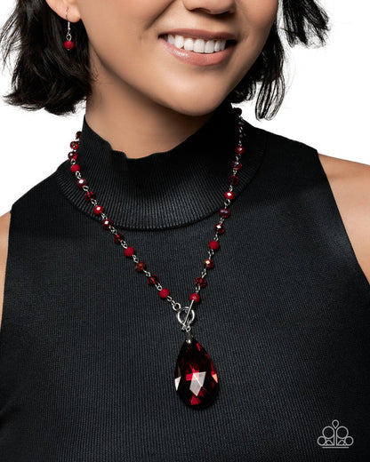 Woman wearing a red beaded necklace with a teardrop pendant on a plain background