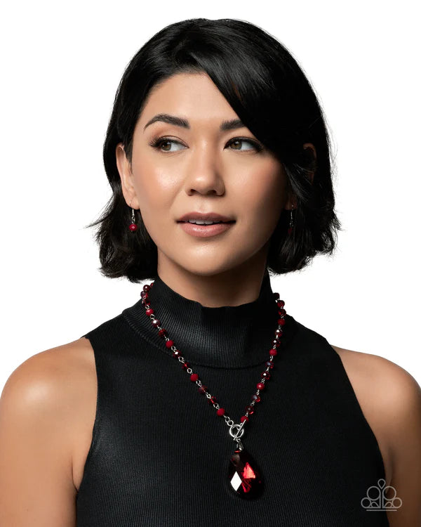 Woman wearing a black turtleneck and red beaded necklace against a white background