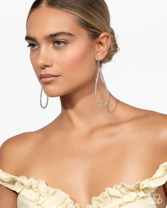 Woman wearing silver hoop earrings against a plain background