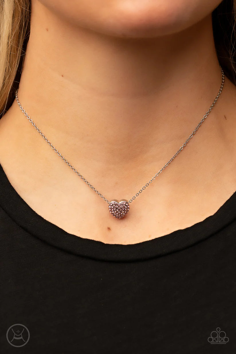 Necklace with a heart-shaped pendant worn by a person against a black background